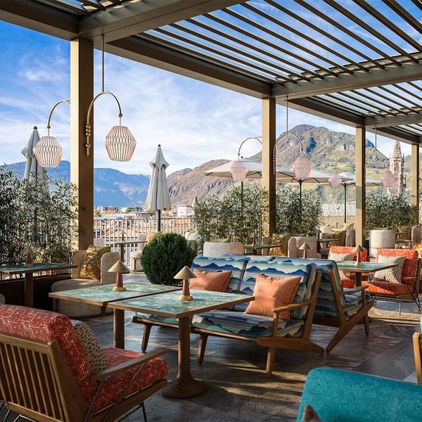 Vanjska terasa restorana s drvenim namještajem, šarenim jastucima, kišobranima i pogledom na planine.