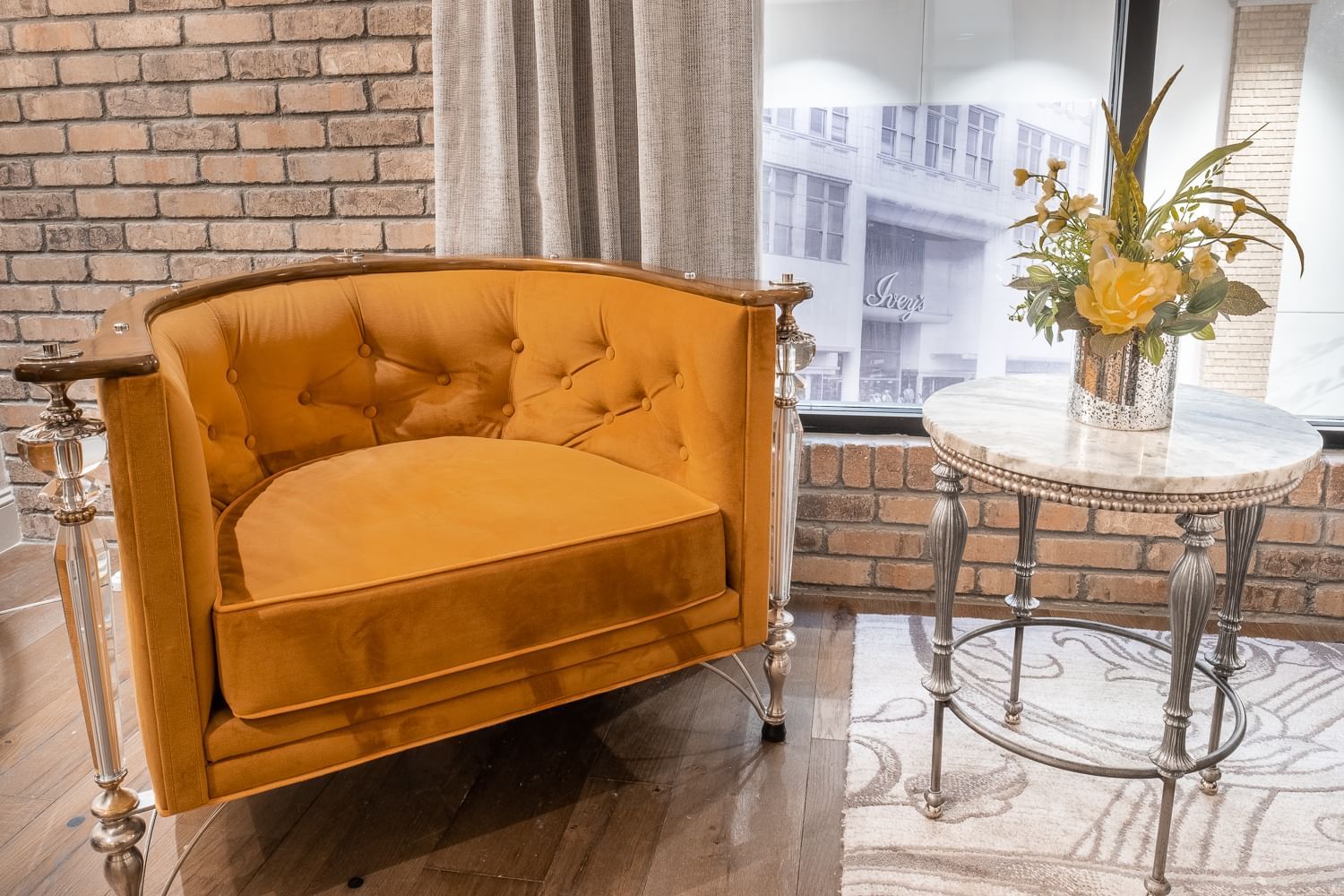 A yellow velvet sofa and a marble side table in a room with a brick wall and window.