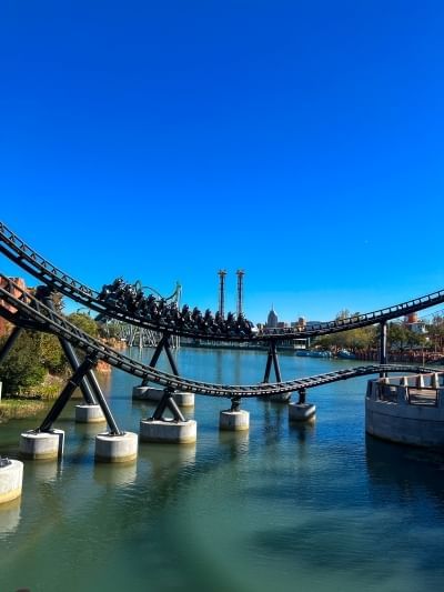 A roller coaster track swoops over a body of water with other rides in the distance. 