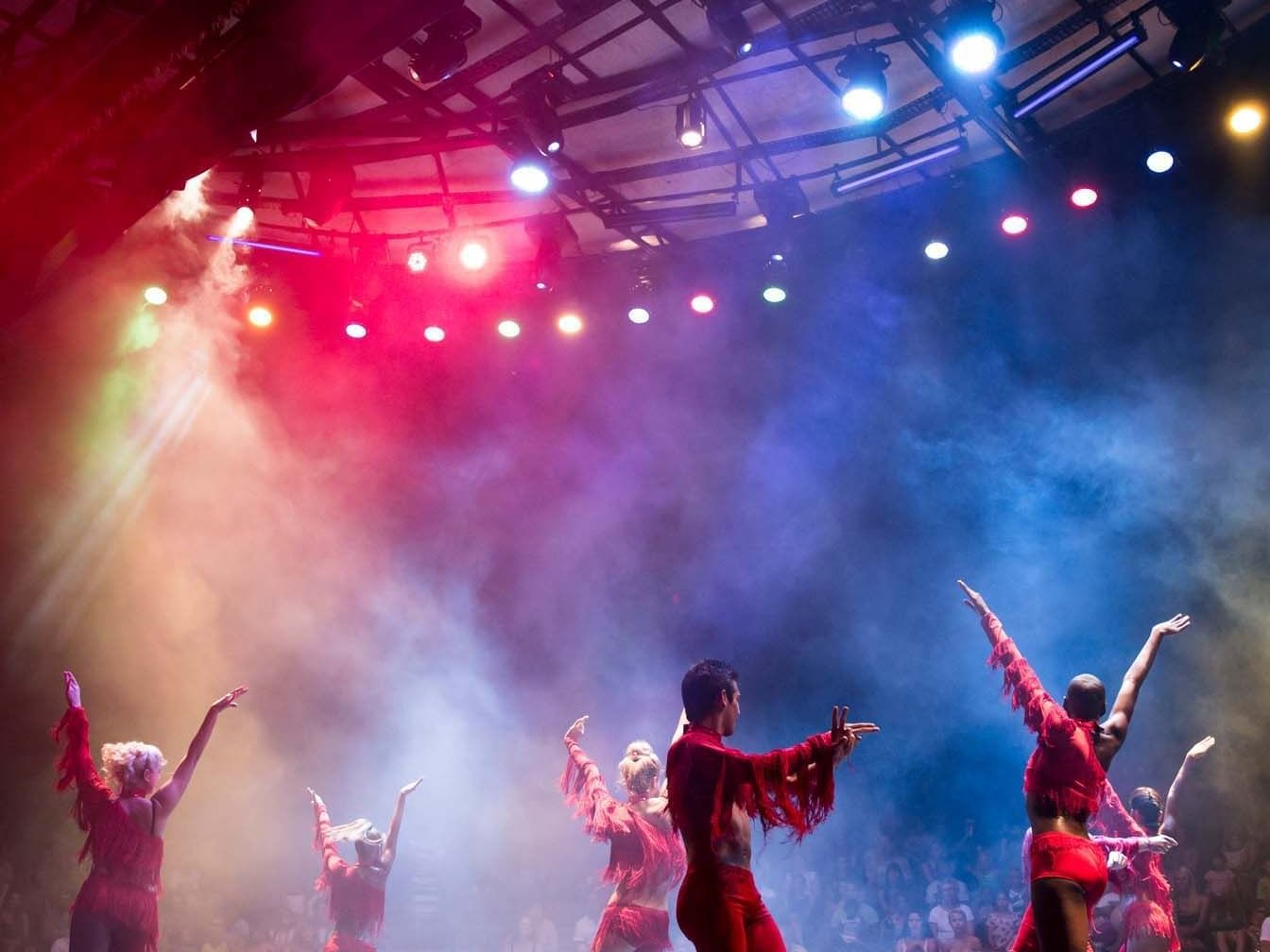 A group of individuals performing on stage with colorful lights at Titanic Deluxe Lara
