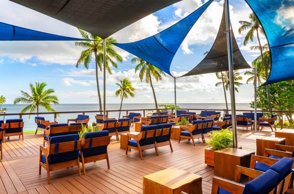 A beachside outdoor lounge with blue chairs under blue triangular canopies at Naviti Resort Fiji Coral Coast