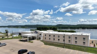Aerial view of Off Shore Resort by the river featuring a parking lot and surrounded by lush green hills in the background