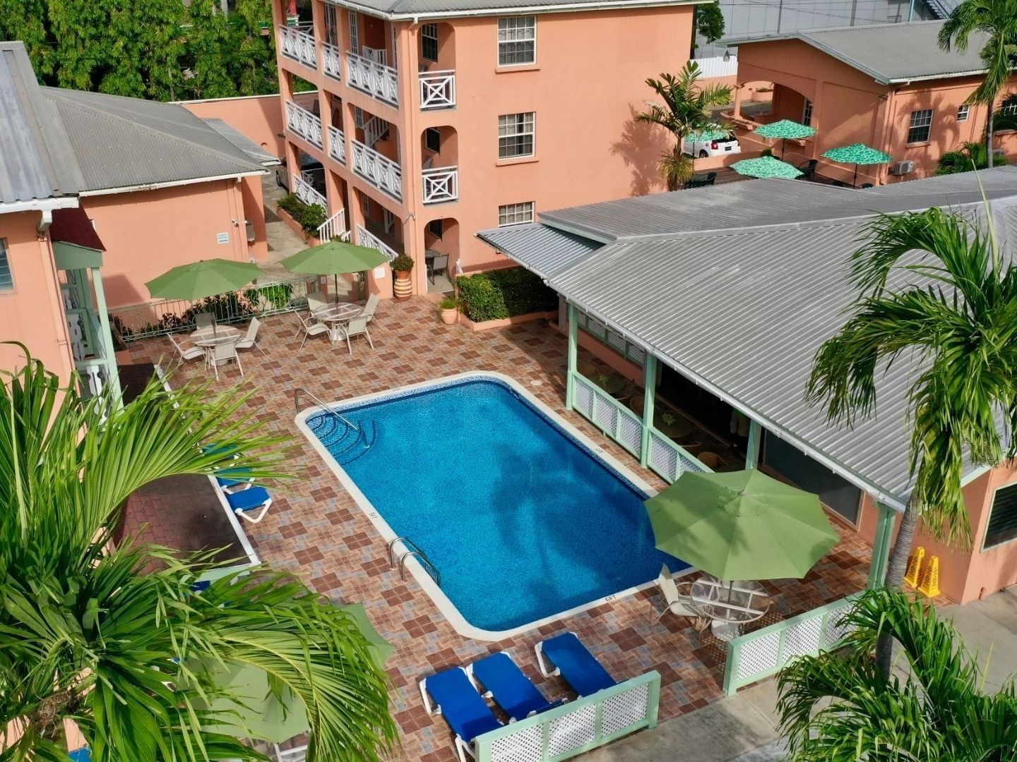 Elevated view of pool with shaded tables and coral buildings surrounded by palms at Worthing Court Apartment Hotel