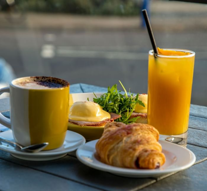 A coffee cup, orange juice, and a plate with a croissant and eggs at The View Hotel Eastbourne