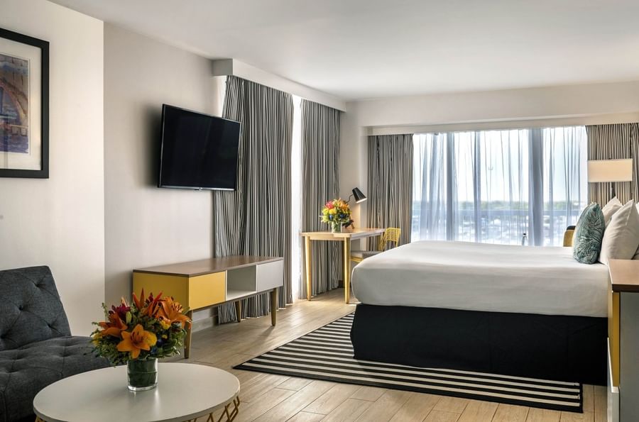 King bed by a desk under a TV near a round table with flowers in Harbour Deluxe Balcony at Warwick Paradise Island Bahamas