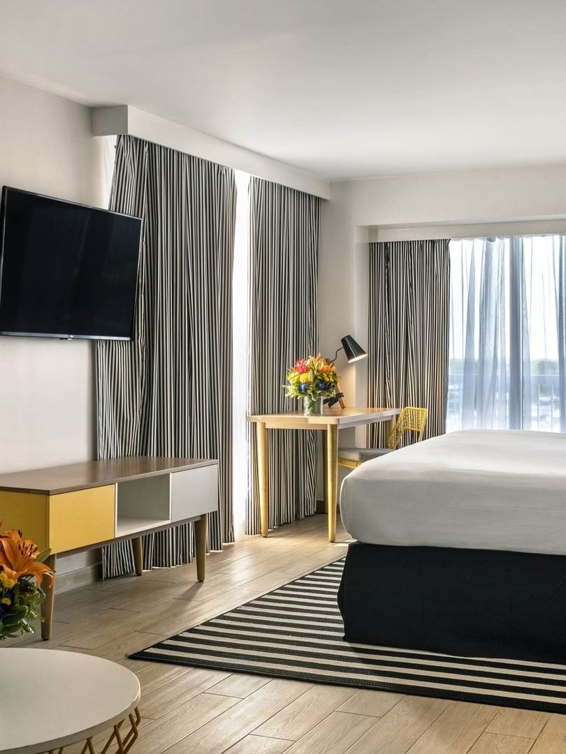 King bed by a striped rug under a TV with a desk and chair in Harbour Premium Balcony at Warwick Paradise Island Bahamas