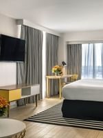 King bed by a striped rug under a TV with a desk and chair in Harbour Premium Balcony at Warwick Paradise Island Bahamas