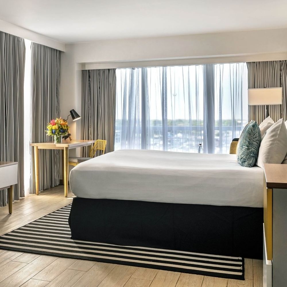 King bed by a striped rug under a TV with a desk and chair in Harbour Premium Balcony at Warwick Paradise Island Bahamas