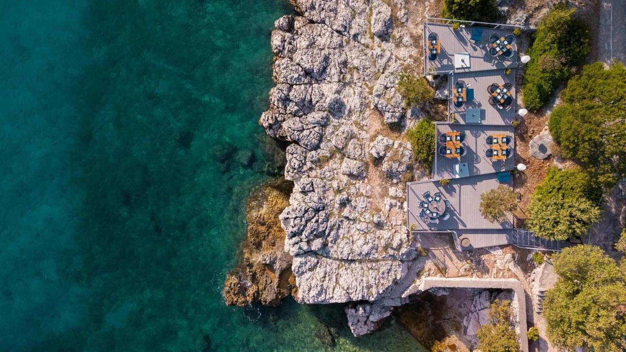Vista aerea di un ristorante sulla scogliera con vista sul mare verde.