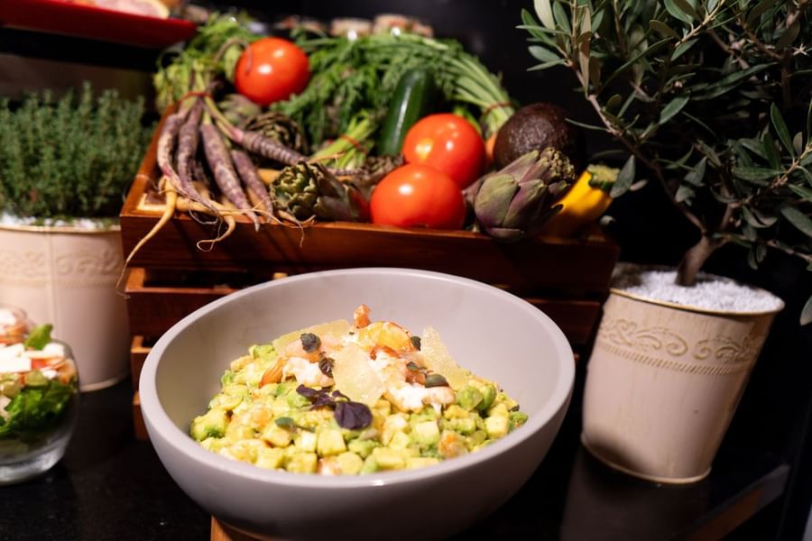 Un bol de salade d'avocat au premier plan, sur fond coloré de légumes frais, au Warwick Paris Champs-Élysées