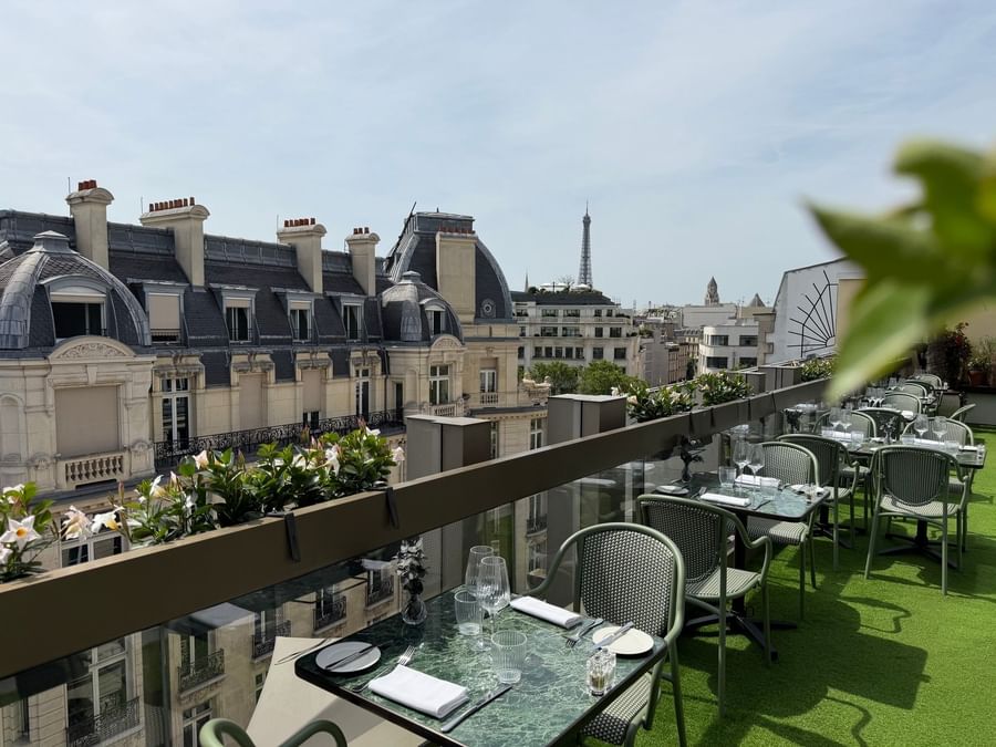 Rooftop dining tables with green chairs by flowers overlooking the Eiffel Tower view at Restaurant, Bar & Terrace Le W
