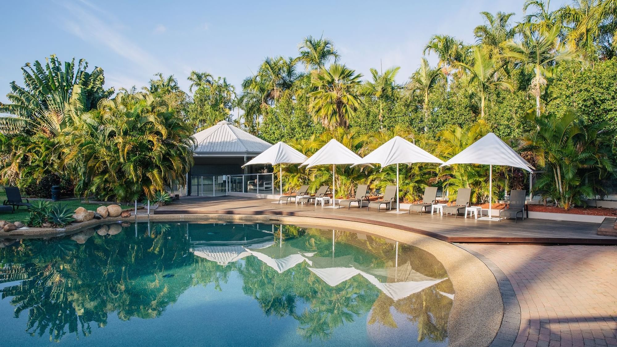 Outdoor pool surrounded by lush greenery, umbrellas, and lounge chairs at Mercure Hotel Townsville