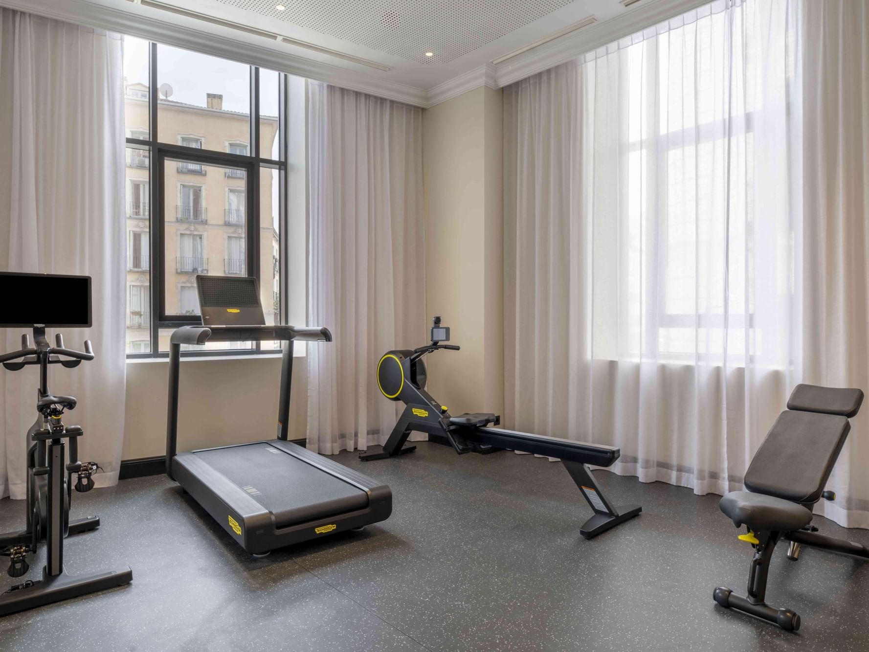 Technogym treadmill and bike by floor-to-ceiling windows with sheer curtains in the fitness center at Urban Hive Madrid