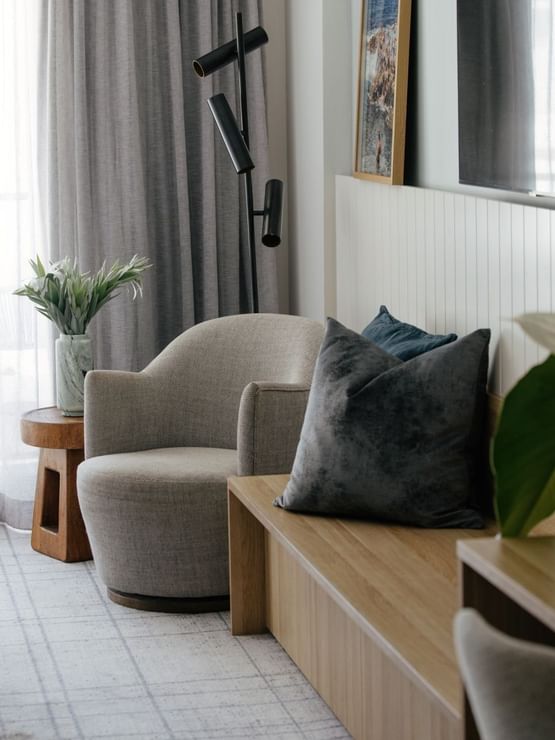 Atrium Twin at Elysium Manly, featuring a grey armchair by a wooden bench under a mounted TV near sheer curtains