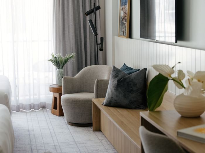 Atrium Twin at Elysium Manly, featuring a grey armchair by a wooden bench under a mounted TV near sheer curtains