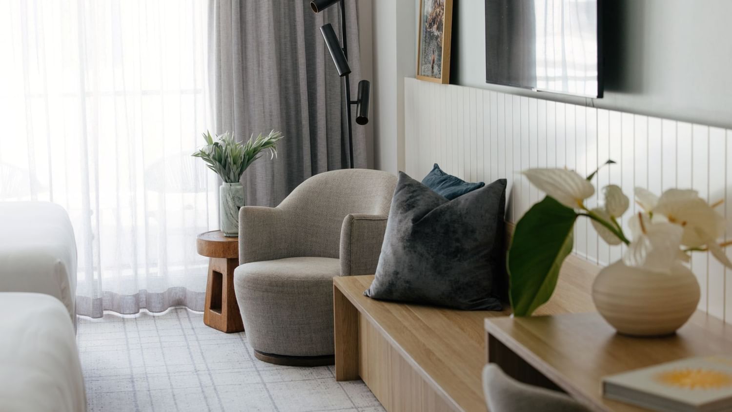 Atrium Twin at Elysium Manly, featuring a grey armchair by a wooden bench under a mounted TV near sheer curtains