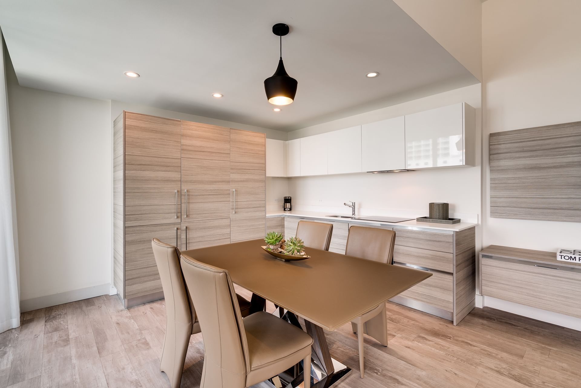 A modern dining area with a kitchenette, featuring a table with four chairs, a kitchenette with white cabinets, and a light wood floor.