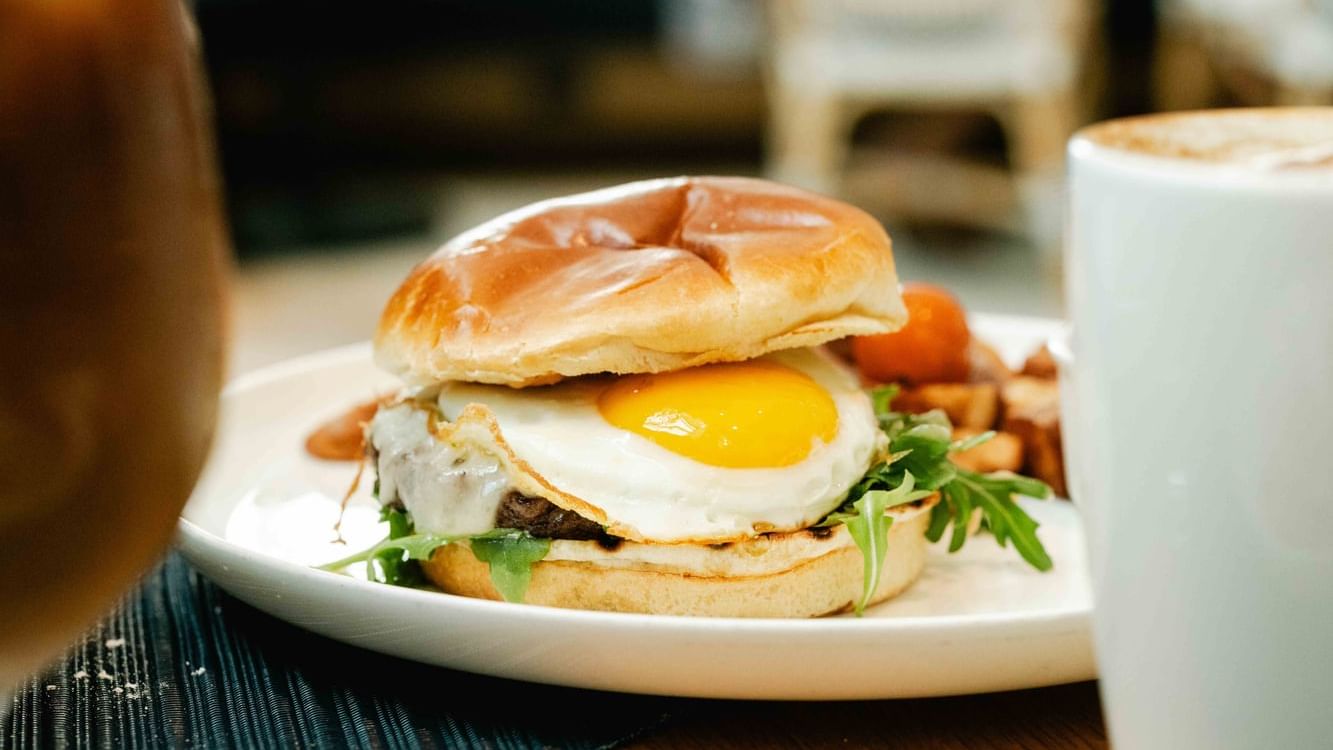 Close-up of a breakfast sandwich with a sunny-side-up egg, leafy greens, with a coffee at The Diplomat Resort