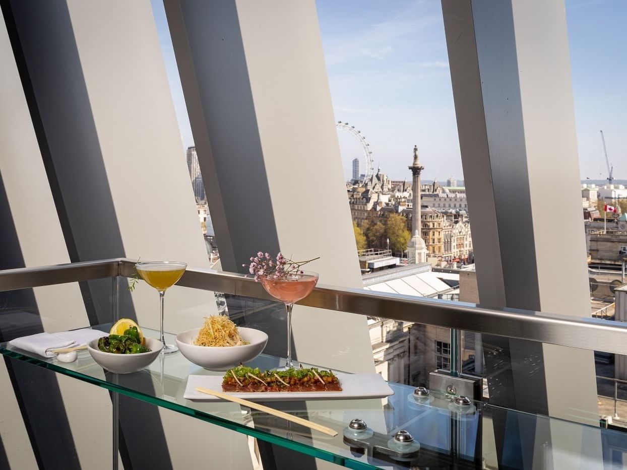 Appetizers & beverages are served by a window with a cityscape at The Londoner Hotel