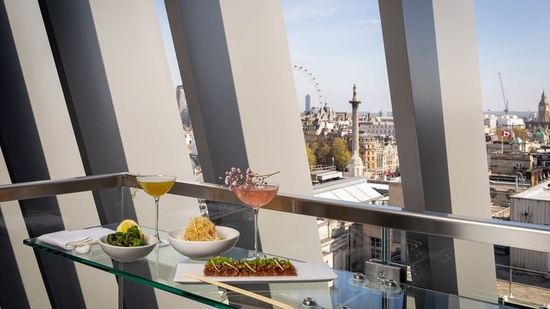 Appetizers & beverages are served by a window with a cityscape at The Londoner Hotel