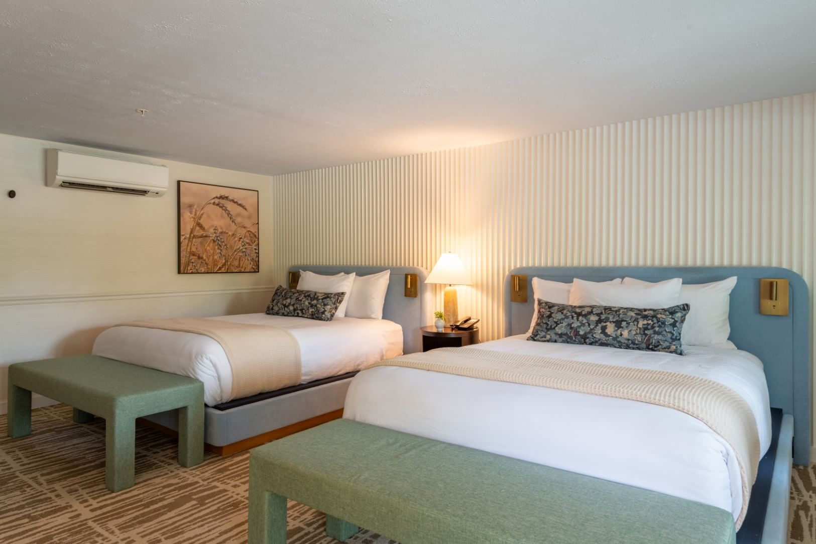 A hotel room with two beds, green benches, and blue headboards.