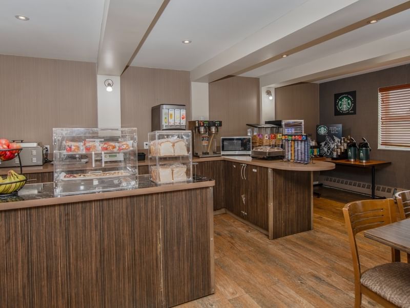 Breakfast room with wooden counters, fruits, pastries, and coffee.