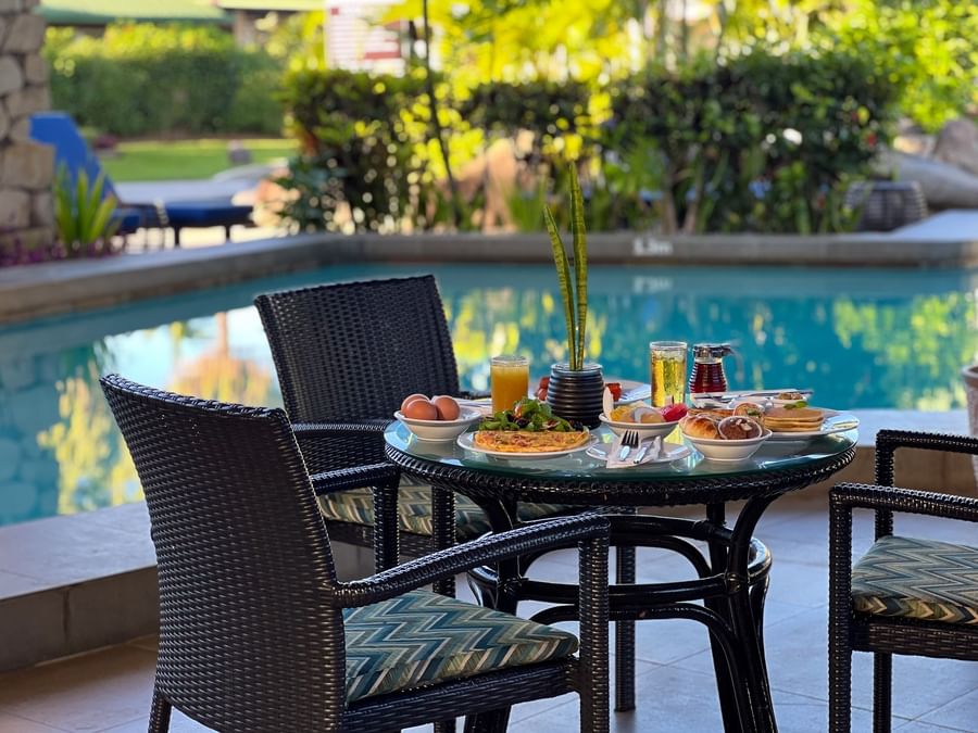 Breakfast spread on a glass table by black wicker chairs near a swimming pool at TokaToka Resort Nadi Fiji
