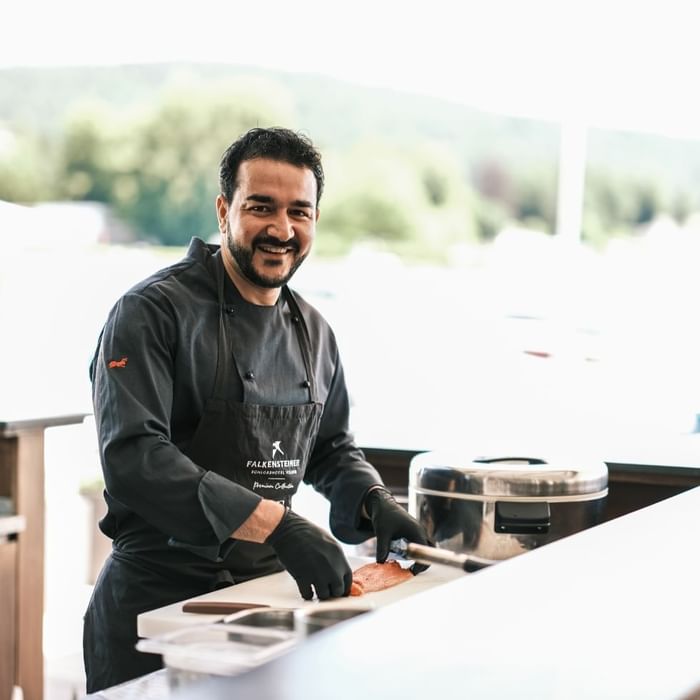 A chef in a black uniform prepping food on a counter at  Falkensteiner Hotels & Residences