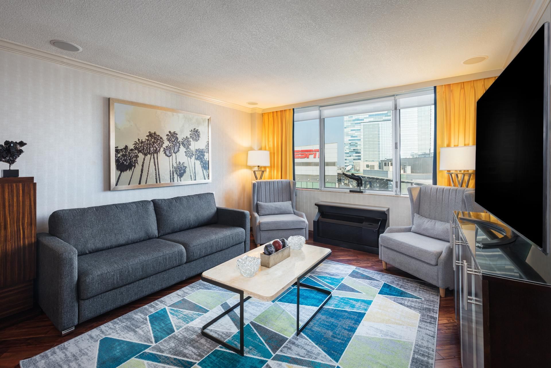 A hotel lobby with a gray sofa, two chairs, a coffee table, and a colorful rug.