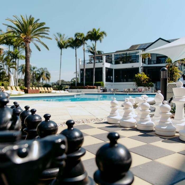 Giant chess set on pool deck with pool and resort building in background.