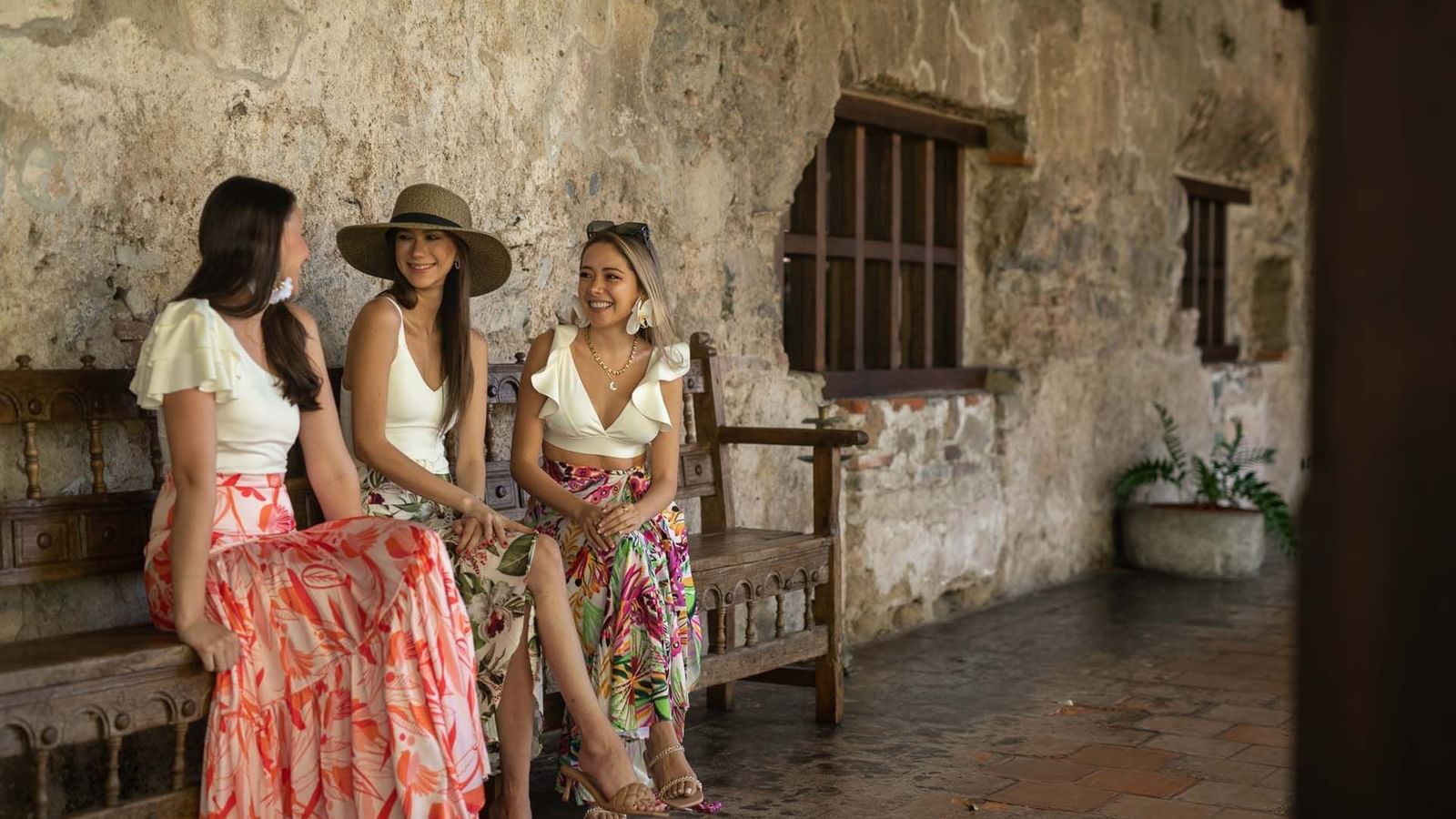 Tres mujeres sonriendo y relajándose en un banco de madera en un patio rústico en Casa Santo Domingo