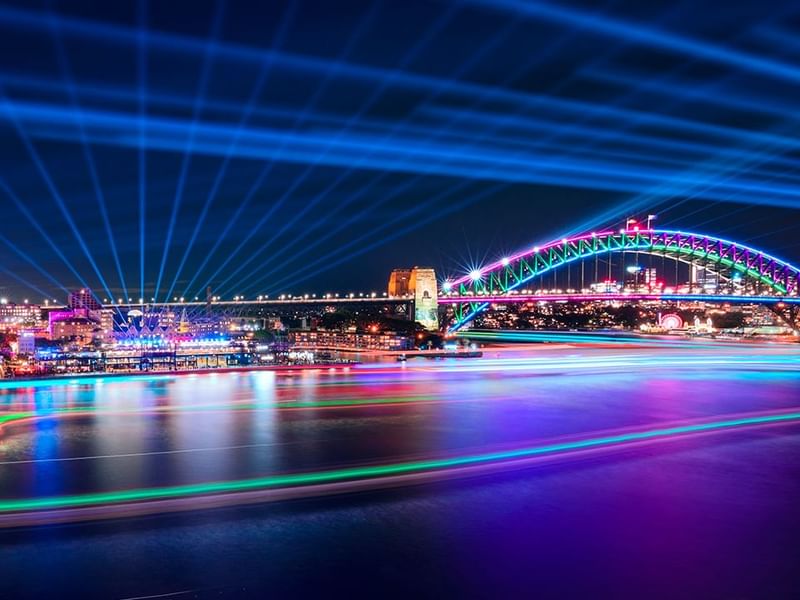 Sydney Harbour Bridge illuminated with rainbow lights over the water at night near Pullman Sydney Hyde Park