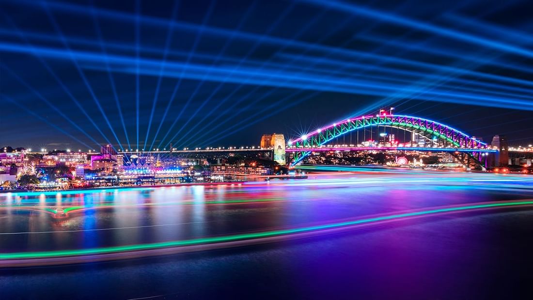 Sydney Harbour Bridge illuminated with rainbow lights over the water at night near Pullman Sydney Hyde Park