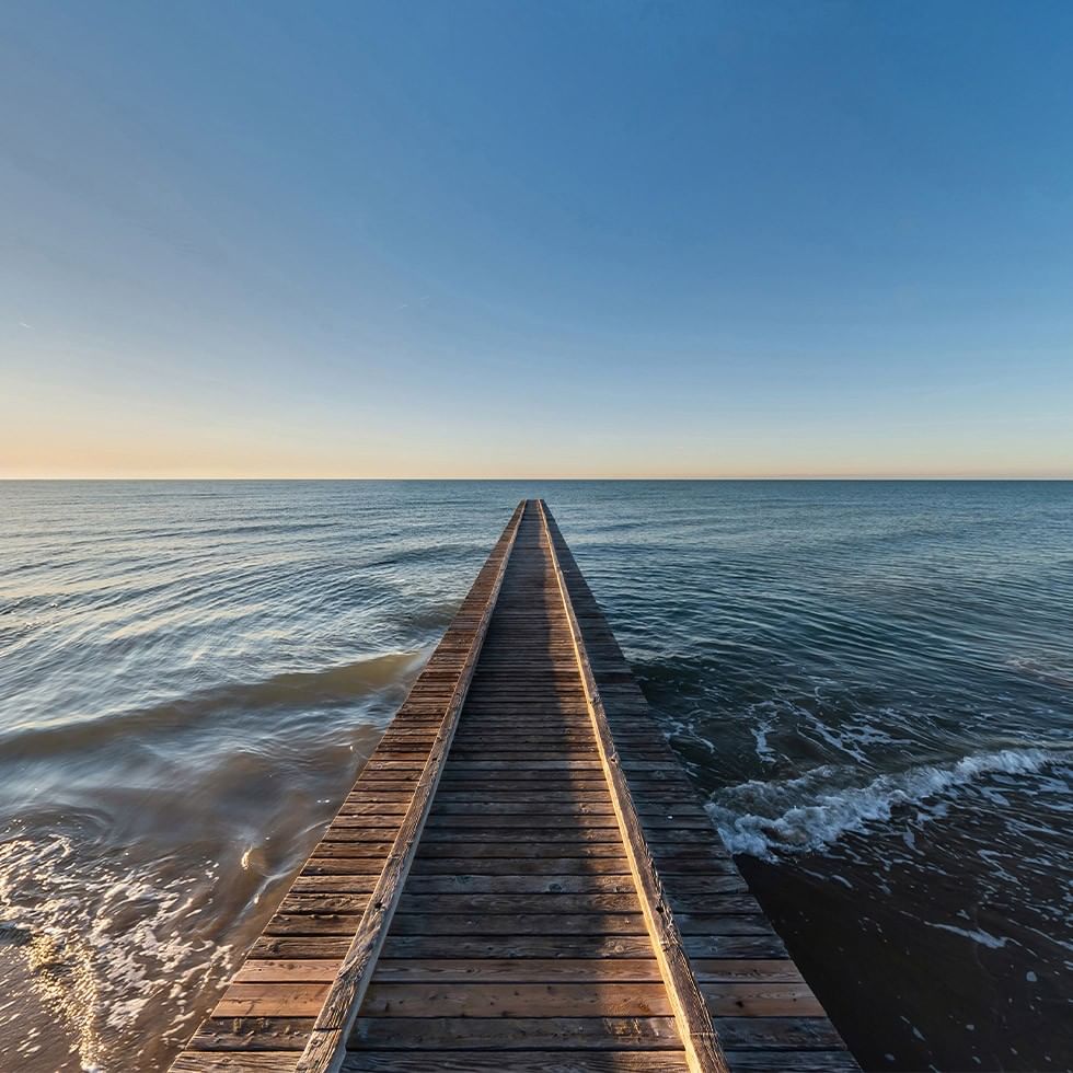 Holzsteg über das Meer, der in der Ferne verschwindet, bei Sonnenuntergang mit blauem Himmel.