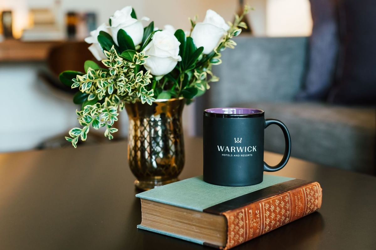 Black coffee mug by a book under white roses in a gold vase at Landingplace Hotels at Warwick Denver