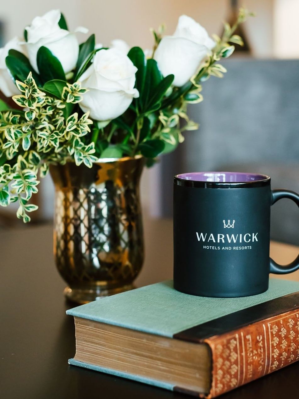 Black coffee mug by a book under white roses in a gold vase at Landingplace Hotels at Warwick Denver