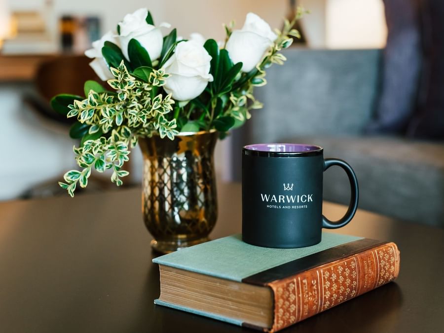 Black coffee mug by a book under white roses in a gold vase at Landingplace Hotels at Warwick Denver
