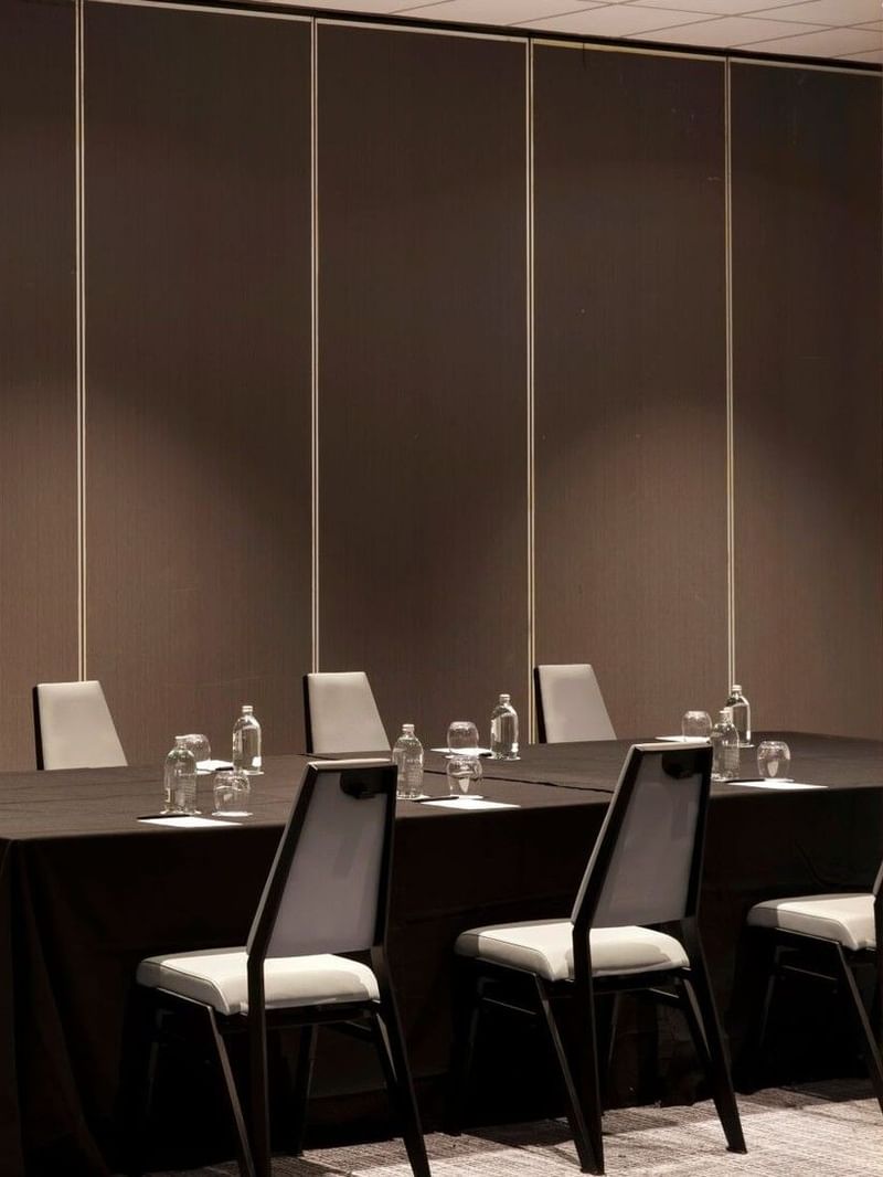 Long dark meeting table at Elysium Manly surrounded by modern grey chairs under a brown panel wall in The Cove Rooms