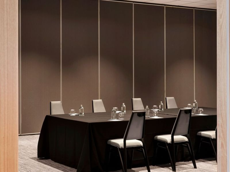 Long dark meeting table at Elysium Manly surrounded by modern grey chairs under a brown panel wall in The Cove Rooms