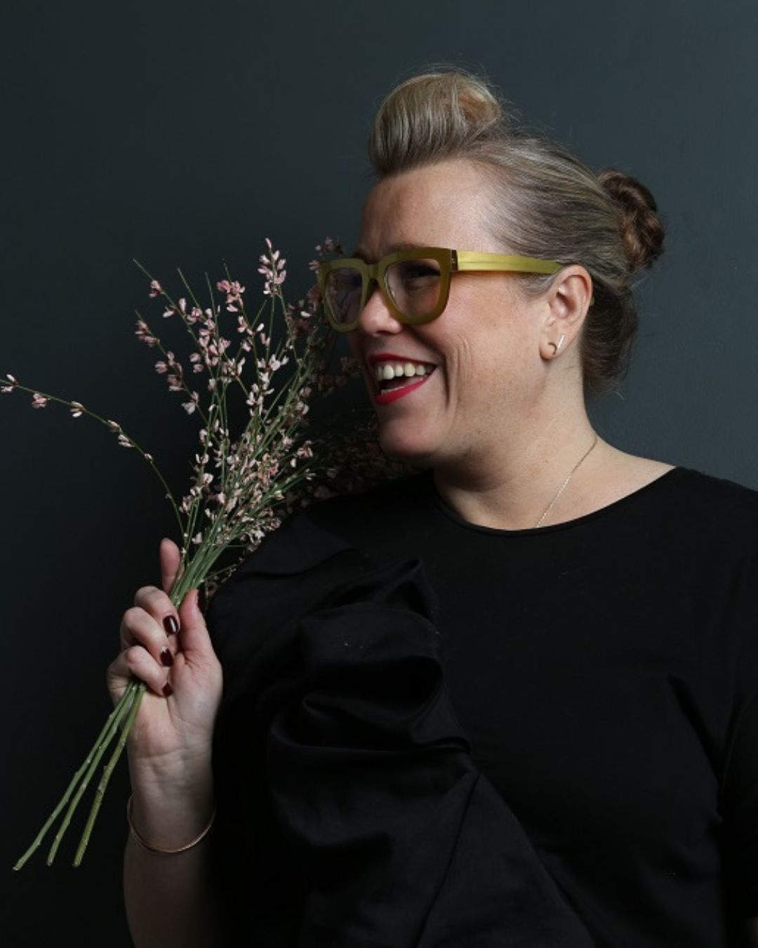 Portrait of a black-dressed woman smiling while holding flowers in a dark background at The Londoner Hotel