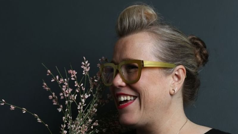 Kate Halfpenny smiling holding flowers and wearing green glasses in an event poster.