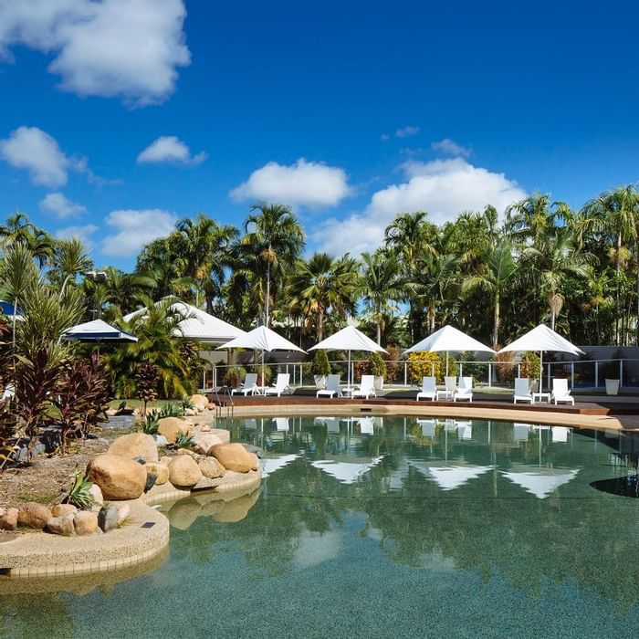 Outdoor large pool area with umbrellas and loungers by the lush greenery at Mercure Townsville