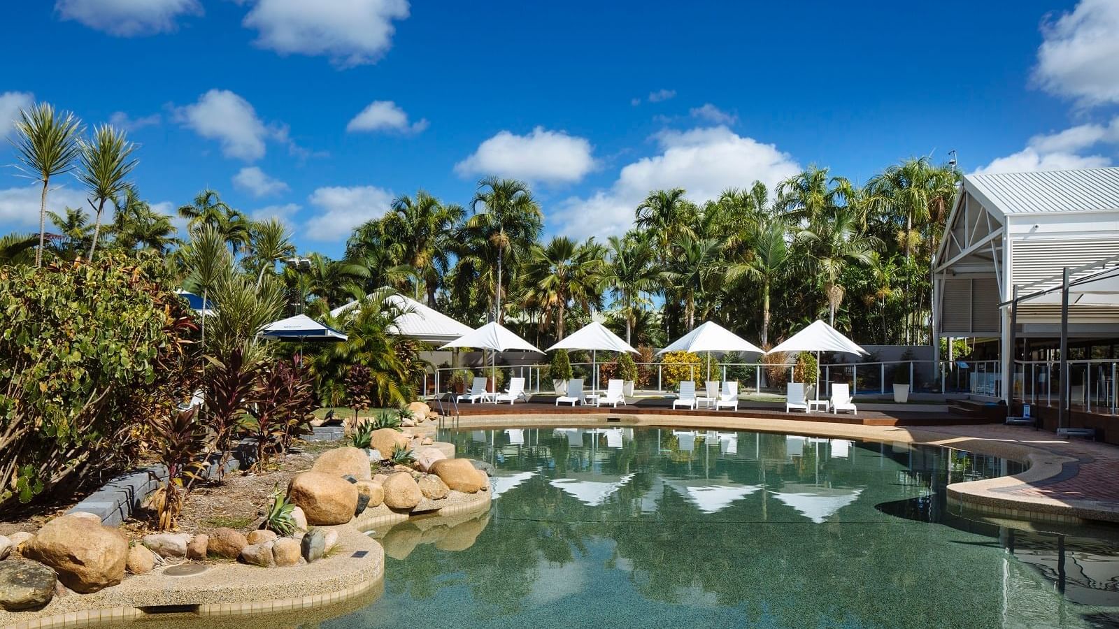 Outdoor large pool area with umbrellas and loungers by the lush greenery at Mercure Townsville