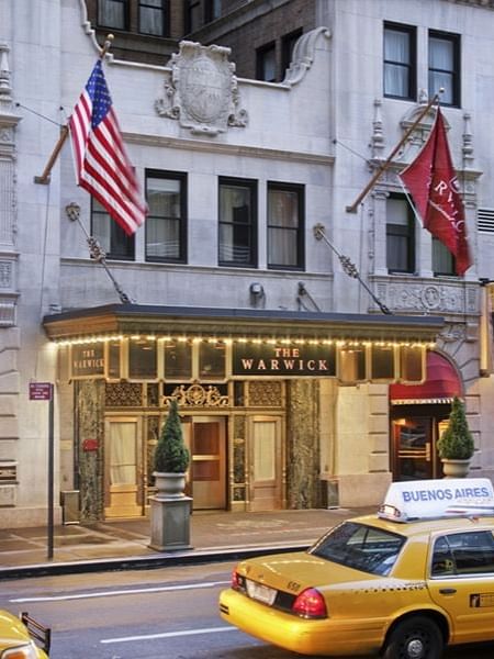 Elegant entrance canopy at Warwick Hotels & Resorts, with flags placed by the door under warm lights