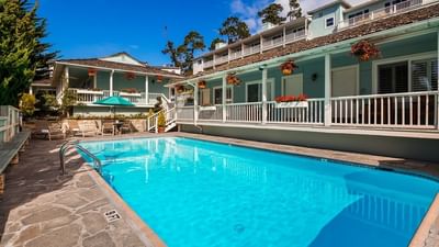 The inviting bright blue swimming pool is surrounded by stone paving and the hotel's blue buildings at Carmel Bay View Inn
