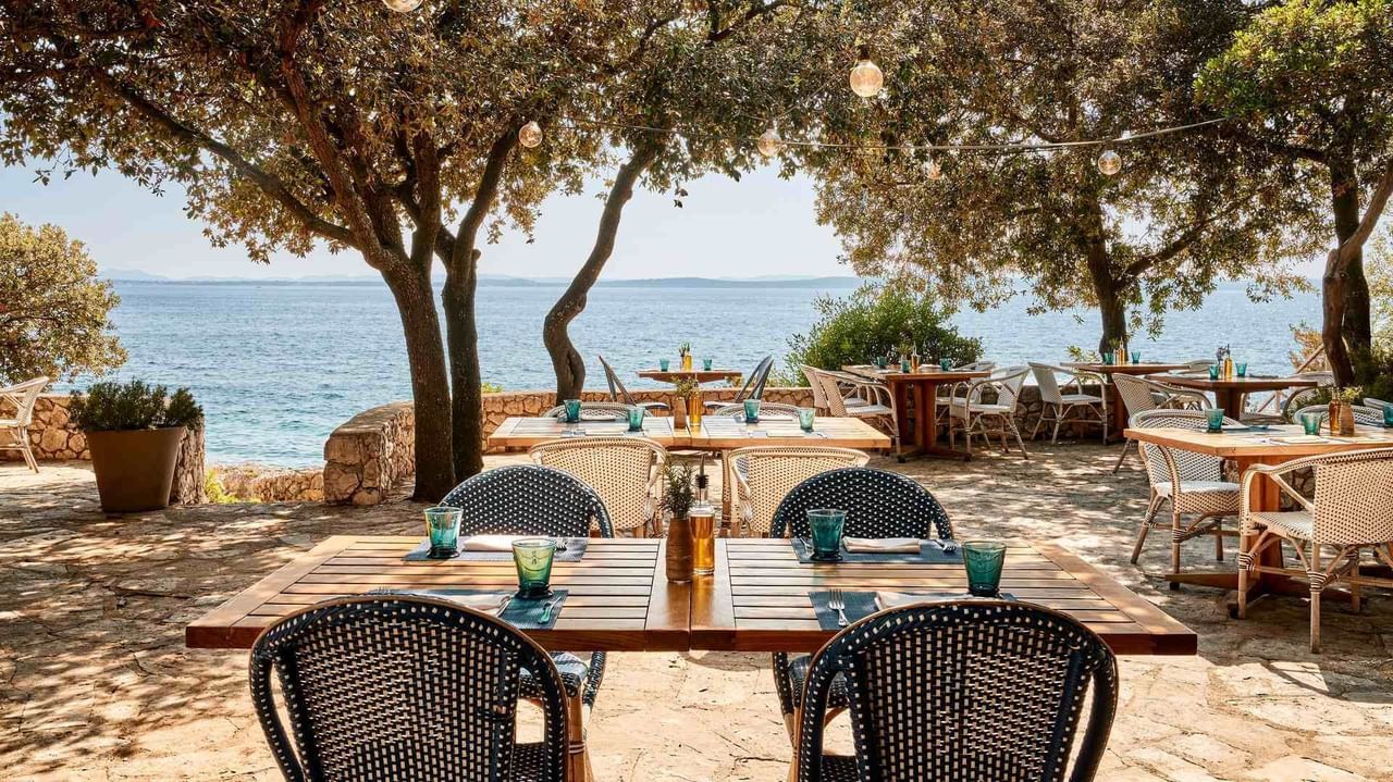 Ristorante all'aperto con tavoli e sedie sotto gli alberi vicino all'acqua.