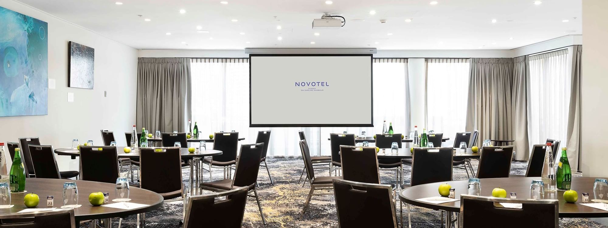 Banquets set up facing the projector screen in The Barossa Room at Novotel Sydney on Darling Harbour