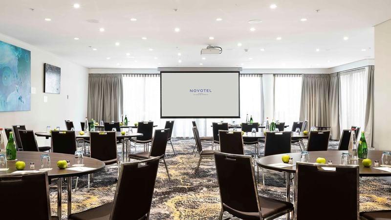 Banquets set up facing the projector screen in The Barossa Room at Novotel Sydney on Darling Harbour