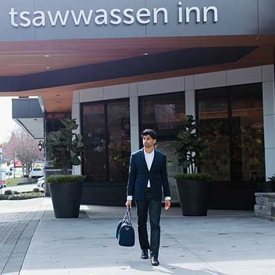 Man in suite walking with a bag in hand in front of Coast Tsawwassen Inn