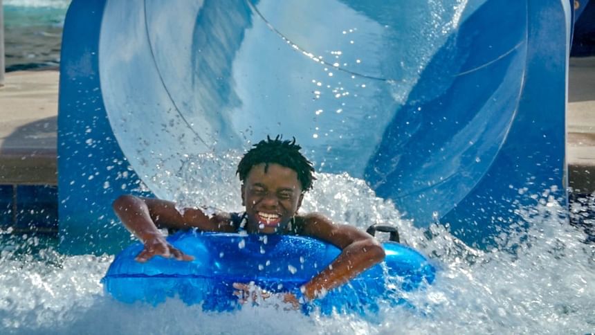 Excited boy splashing into the water on a blue inner tube in the water park at Margaritaville Resort Biloxi